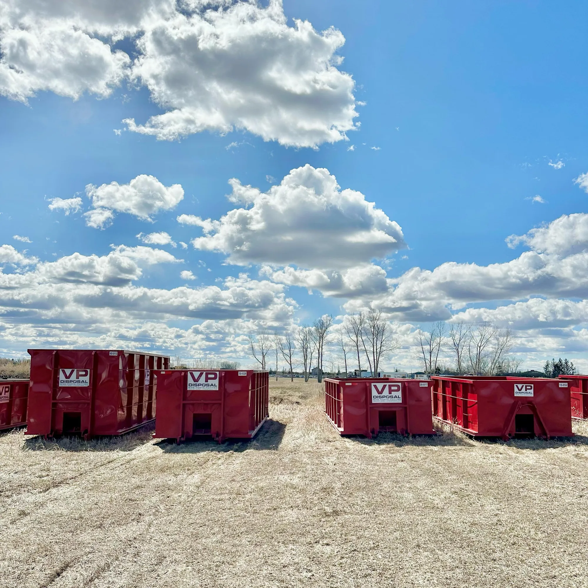 Four red VP Disposal roll-off bins of different sizes lined up in the yard under a blue sky
